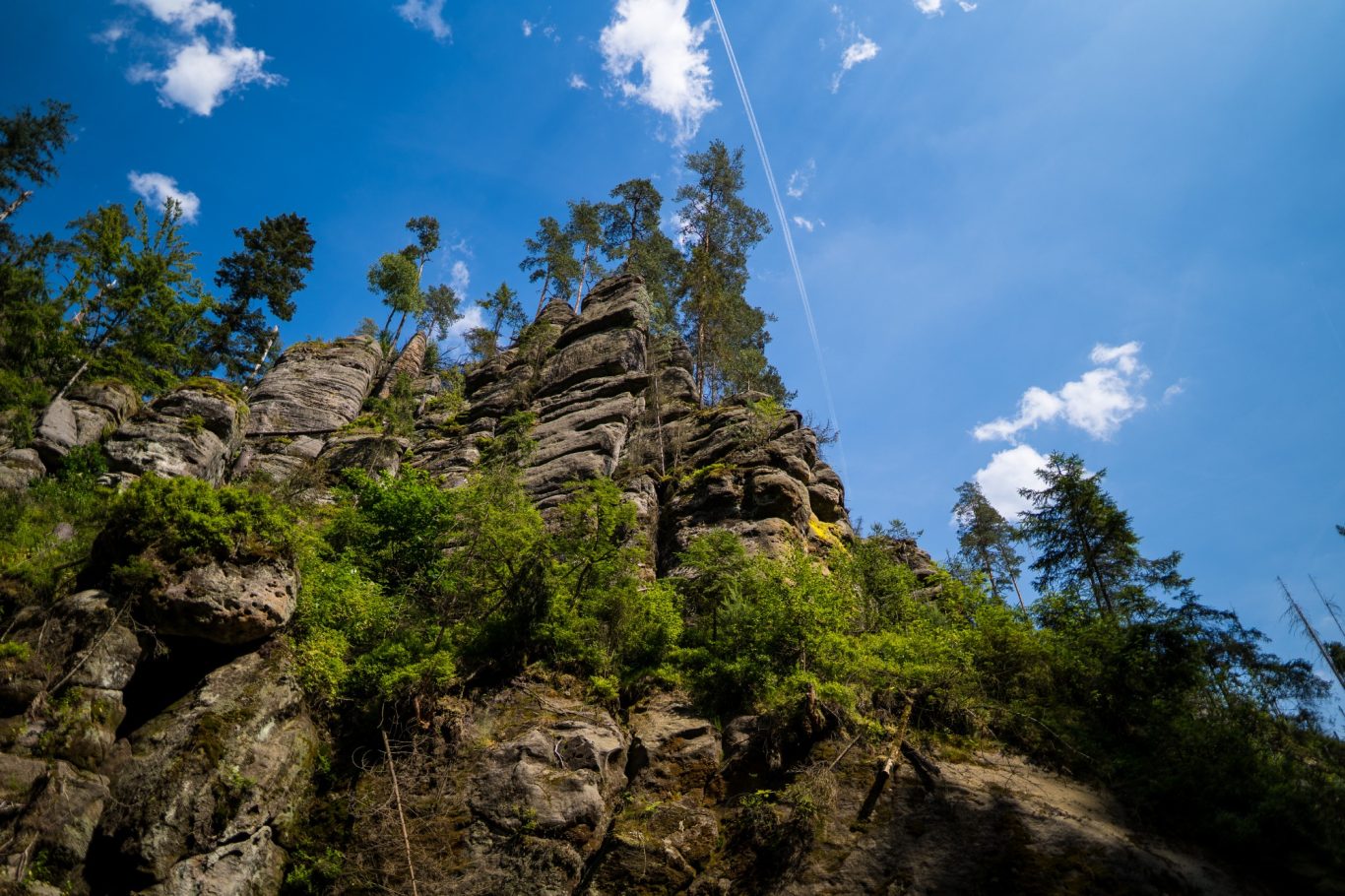 Gebirge Hochaufragende Felsen unter blauem Himmel, umgeben von Bäumen und einigen Wolken.